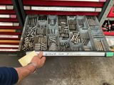 un homme tenant un morceau de métal devant un tiroir rempli de vis