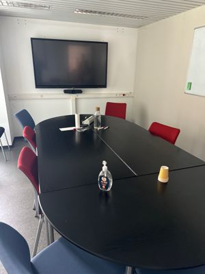 une table noire avec des chaises rouges et une télévision en arrière-plan