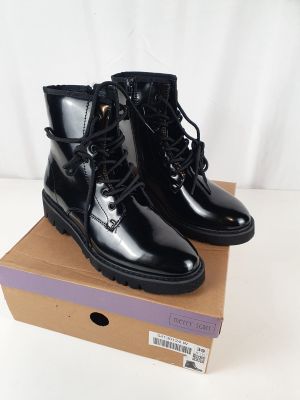 des bottes en cuir noir à lacets, avec des semelles en caoutchouc, posées sur une boîte en carton