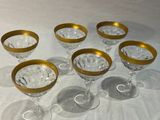 six verres à vin à bord doré posés sur une nappe blanche