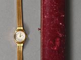 une montre en or et un étui rouge posés sur une table