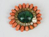 un gros plan sur une broche ornée de perles et d'une pierre verte