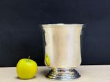 a green apple next to a silver cup on a table