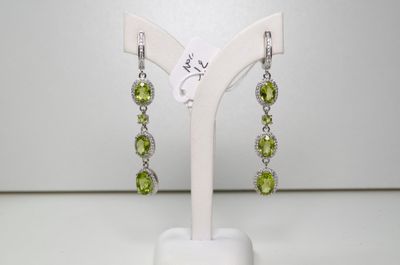 une paire de boucles d'oreilles en péridot et diamants, exposée sur un présentoir blanc