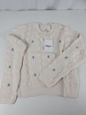 Le pull est blanc et comporte des boutons bleus.