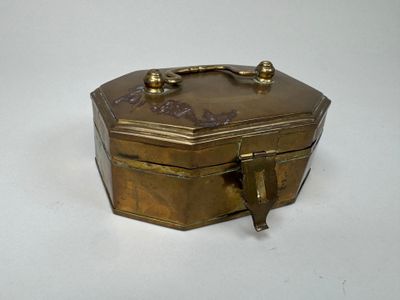 une petite boîte en laiton munie d'une poignée, posée sur une surface blanche