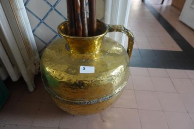 a gold vase with sticks in it sitting on the floor