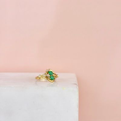 un gros plan d'une bague en or sertie de pierres vertes, posée sur un bloc de marbre blanc