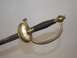 a gold colored sword with a black handle on a white surface