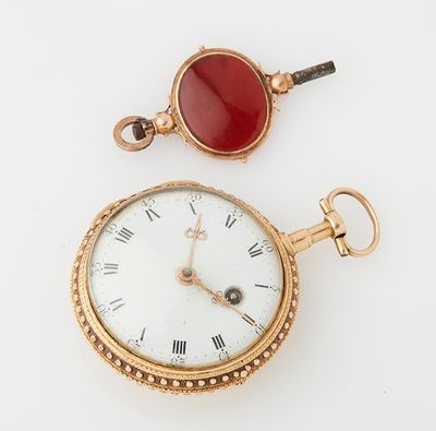 a gold pocket watch with a red stone on the face