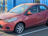 une voiture rouge garée sur un parking, avec des vélos en arrière-plan