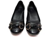 des chaussures en cuir noir ornées de boucles dorées, posées sur un fond blanc