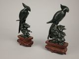 pair of black birds sitting on a branch on top of a wooden base