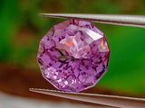 quelqu'un tient une pince dans laquelle est sertie un diamant violet