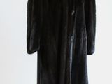 un manteau de fourrure noir posé sur un mannequin, devant un mur blanc