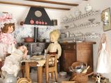 two dolls sitting at a table in a doll house