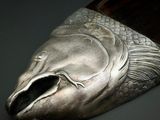 une tête de poisson argentée posée sur une cuillère en bois, sur une table