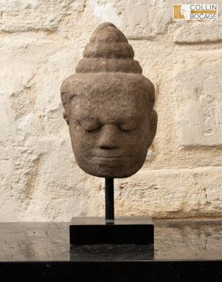 sculpture représentant une tête posée sur un socle devant un mur de pierre