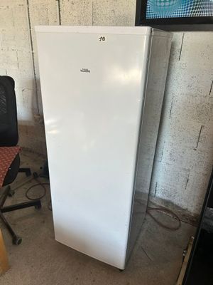 un réfrigérateur blanc posé dans une pièce, à côté d'une chaise