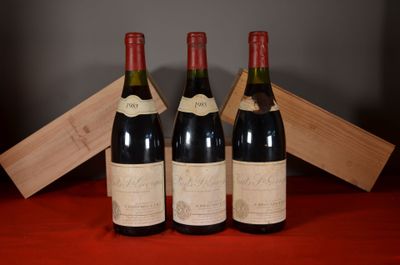 three bottles of wine sit on a red cloth with a wooden box in the background