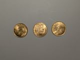 trois pièces d'or sont représentées en ligne sur une surface grise