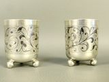 two silver cups with designs on them sitting next to each other