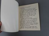 a hand holding an open book with a handwritten poem on it