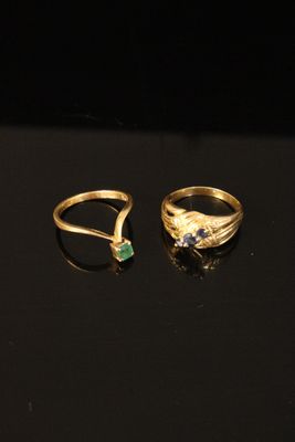 two gold rings with emerald stones on a black surface