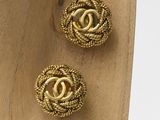 two pairs of gold toned chanel earrings on a wooden stand