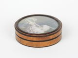 une boîte ovale en bois sur laquelle figure l'image d'une femme en robe blanche