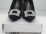 une paire de chaussures noires ornées de cristaux, posée sur une boîte