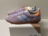 des baskets Adidas violettes posées sur une boîte, sur une surface blanche