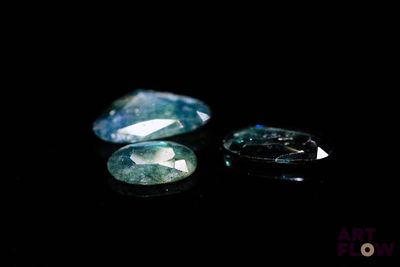 two green sapphires on a black surface with a black background