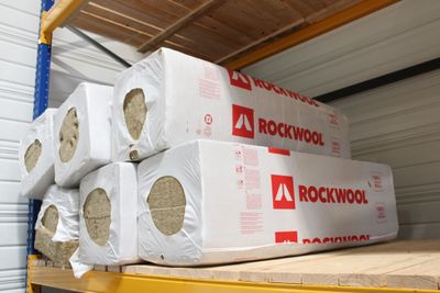 Plusieurs rouleaux de laine de roche sont empilés sur une étagère dans un local de stockage