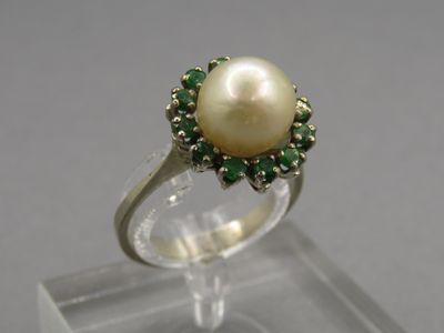 un gros plan d'une bague ornée d'une perle et de pierres vertes