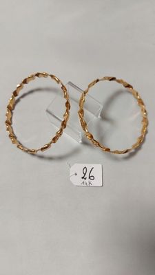 une paire de boucles d'oreilles en or posées sur une surface blanche