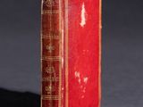 an old red book sitting on top of a table next to a black background