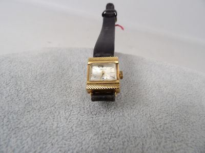 une montre en or avec un bracelet noir sur un fond blanc