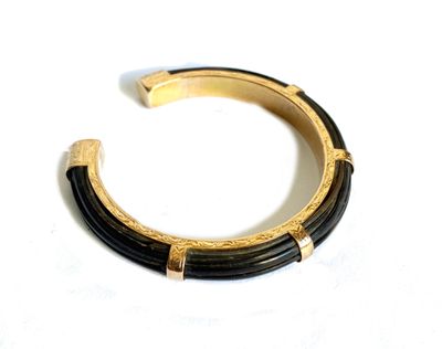 une image représentant un bracelet noir et doré posé sur une surface blanche