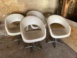 trois chaises blanches posées sur un sol en béton, près d'un mur