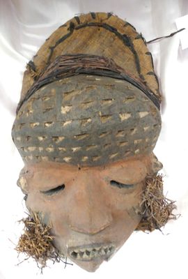 un masque en bois posé sur une surface blanche, entouré d'un fil métallique