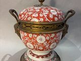 a red and white vase with a gold lid