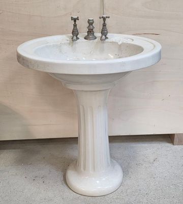 a white pedestal sink with two faucets on it