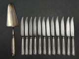 six silverplated knives and a fork on a black surface