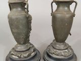 pair of antique bronze vases with handles on pedestals on a white background