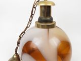brown and white glass ornament with a brass bell on a chain