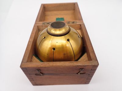 une cloche ancienne en laiton, posée dans une boîte en bois sur une surface blanche