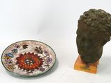 une statue représentant une tête, à côté d'une assiette ornée d'un motif floral