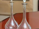 two glass decanters sitting on a table with a picture in the background
