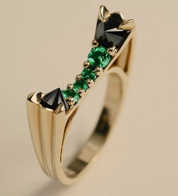 un gros plan d'une bague en or sertie de pierres noires et vertes